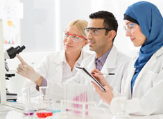 A diverse group of scientists in labcoats, one taking notes and the other looking out of frame